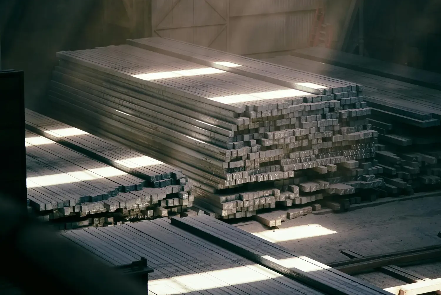 Sunlight streaming through an industrial warehouse highlighting stacked metal beams.